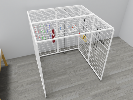 Angled view of the Summit Sensory Gym Universal Exercise Unit, featuring a sturdy white metal grid structure. Inside the cage are therapy tools, including colorful resistance bands, a red padded support, white cone-shaped accessories with hooks, and yellow handles attached to ropes. The cage is positioned on a light gray wood-style floor in a bright, minimalistic therapy setting with part of a wooden table visible in the corner.